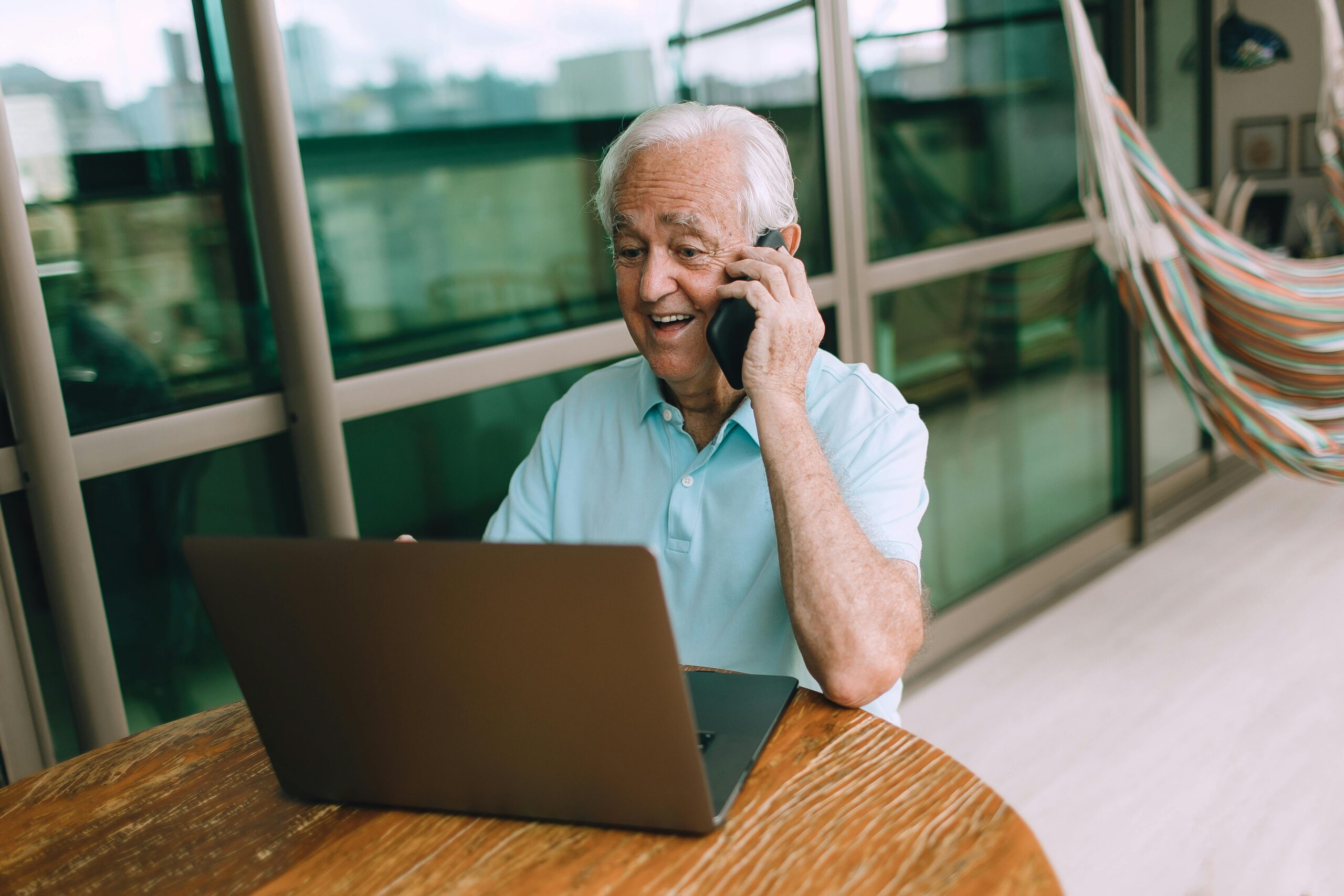Elderly man in casual setting using a laptop and smartphone indoors, reflecting modern communication.