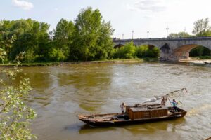A traditional wooden boat sails along the Loire River under a historic stone bridge.