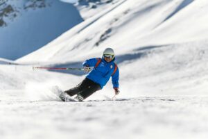 A skier carves down a sunlit snowy slope wearing protective gear. Perfect for winter sports themes.